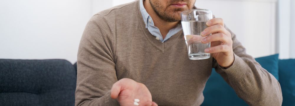 Man sipping water before taking medication with pills in his hand