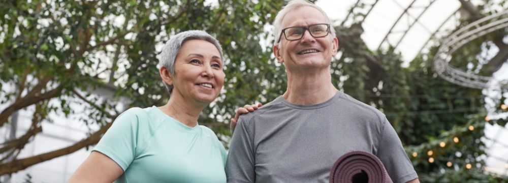 Older man and woman holding yoga mats while smiling, woman hand on mans shoulder